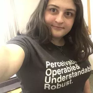 Carly wears a shirt with the text "Perceivable & Operable & Understandable & Robust". She has light skin, shoulder-length brown hair and big eyes. 